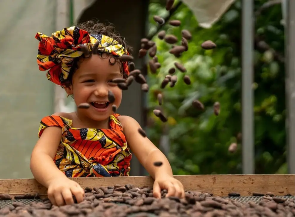 A laughing child tossing cacao beans over a drying bed