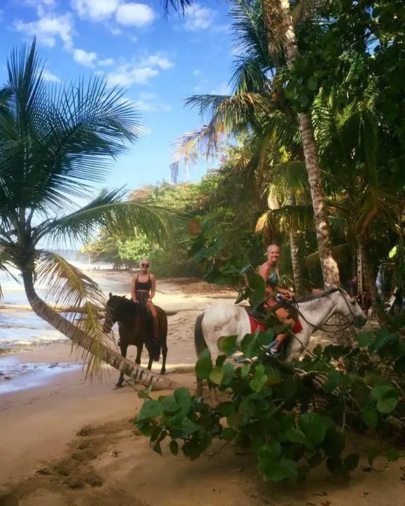 Two Caribe Horse riders on a palm-lined beach at the edge of the jungle